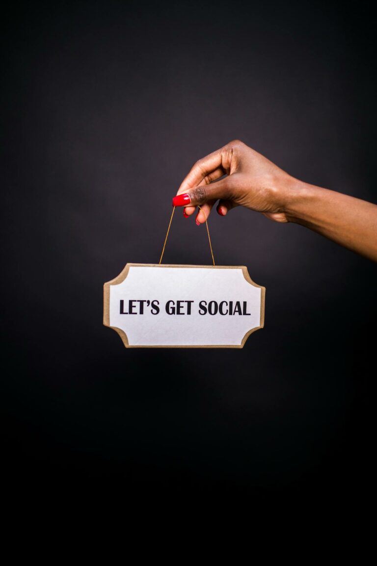 Close-up of a hand holding a sign with 'Let's Get Social' on a dark background.