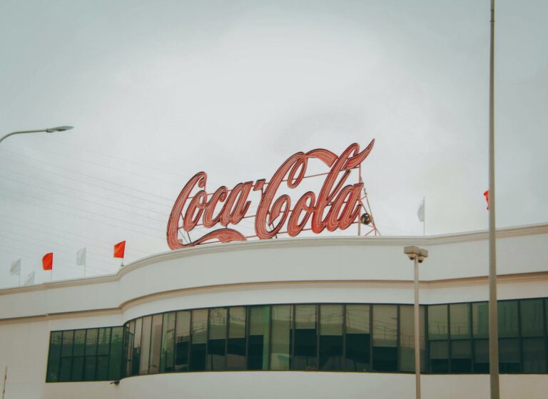 Exterior view of Coca-Cola factory with iconic red sign atop the modern building.